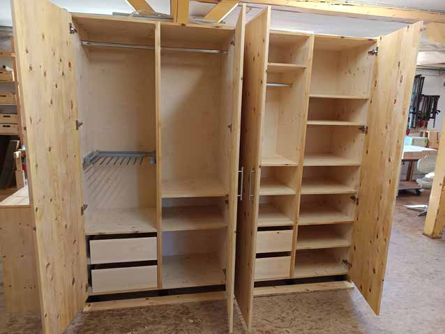 Ein großer, offener Kleiderschrank aus hellem Holz mit Kleiderstangen, Fächern, Schubladen und einem Schuhregal.