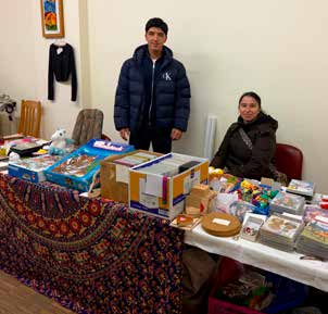 Ein Verkaufsstand mit Spielen, Büchern und Kleinigkeiten, dahinter stehen ein junger Mann und eine junge Frau.