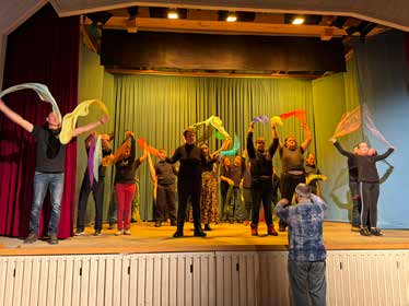 Tänzerinnen und Tänzer schwenken bunte Tücher auf der Bühne.