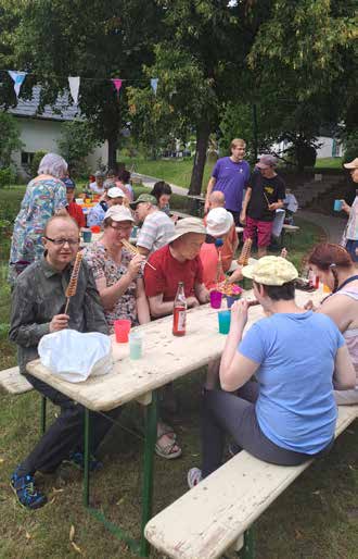 Gäste sitzen an Biertischen im Schatten der Bäume, trinken und essen, im Hintergrund hängen Wimpel.