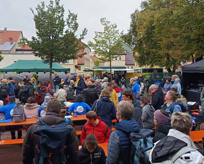 Viele Menschen sitzen an Biertischen auf dem Marktplatz vor der Bühne, dahinter Bäume und Häuser.